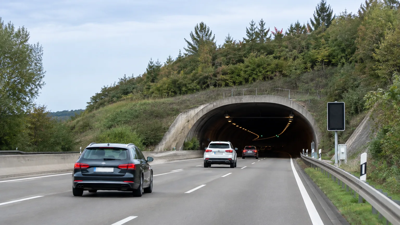 Autos nähern sich einer Tunneleinfahrt zwischen bewachsenen Böschungen.