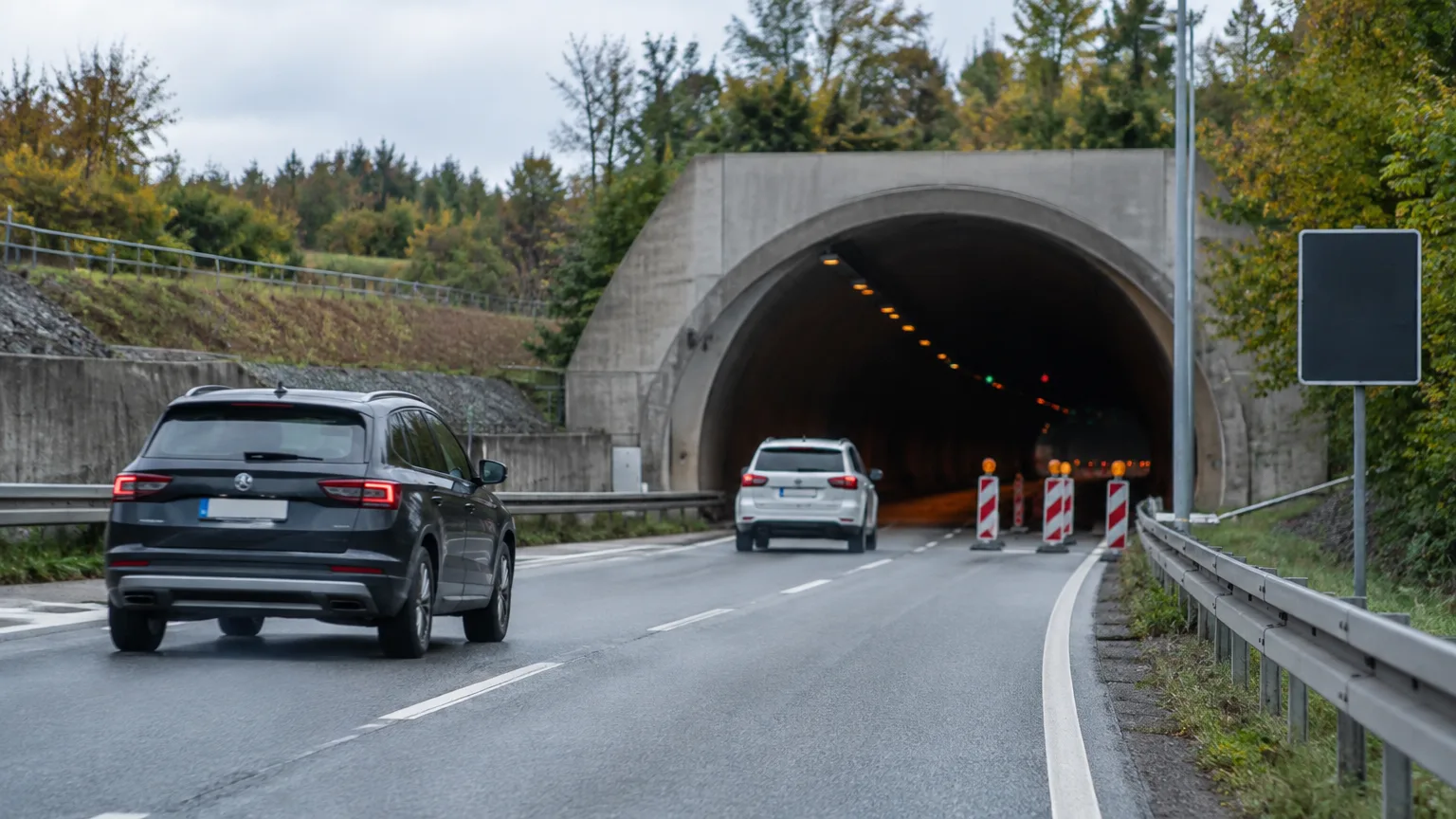 Autos stehen vor einer Tunneleinfahrt; am Fahrbahnrand sind orangefarbene Leitkegel aufgestellt.